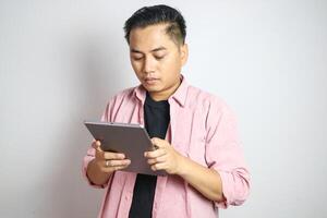 Adult Asian man smiling confident while working using his mobile tablet gadget photo