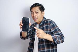 Happy Asian man showing and pointing finger to smartphone mockup of blank screen isolated on white background. photo