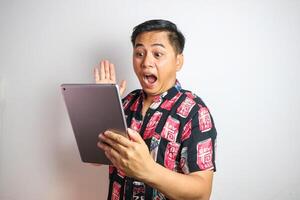 Smiling traveler tourist Asian man in casual clothes holding tablet PC computer and showing thumbs up gesture on white background. Passenger traveling on weekends. Air flight journey concept photo