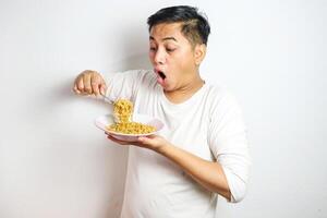 Asian Man grasping and lifting up Noodles Hungrily from Bowl using fork. Hungry Asian Man Devours Delicious Noodles photo