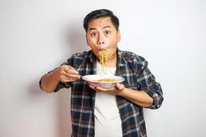 Young handsome trendy asian man eating yummy hot and spicy instant noodle using fork isolated on white background. Asian guy servile end of the month with cheap food. photo