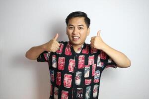 Young asian man wearing casual beach style shirt over white background approving doing positive gesture with hand, thumbs up smiling and happy for success. Winner gesture. photo