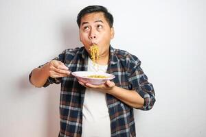 Young handsome trendy asian man eating yummy hot and spicy instant noodle using fork isolated on white background. Asian guy servile end of the month with cheap food. photo