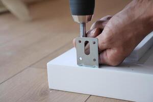 A person is using a power drill effectively to secure a metal bracket onto a clean white surface photo