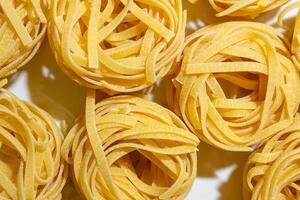 Uncooked Egg-Based Fettuccine Pasta. A Culinary Canvas of Ribbon-Shaped Macaroni, Creating a Lively and Textured Background for Gourmet Cooking. Dry Pasta. Raw Macaroni - Top View, Flat Lay photo