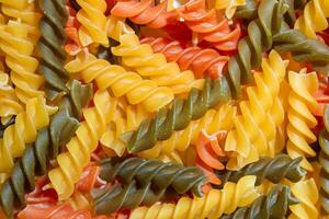 Uncooked Vibrant Colored Fusilli Pasta. A Mesmerizing Culinary Canvas of Multicolored Spirals, Creating a Lively and Textured Background for Gourmet Cooking. Colored Dry Pasta. Raw Macaroni photo