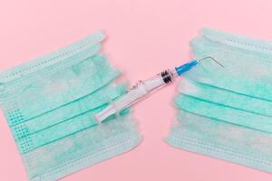 Anti Vaccine Movement and Anti Mask Concept - Broken Medical Syringe and Green Torn Medical Face Mask on the Pink Background. Pandemic and Lockdown End - Top View, Flat Lay photo