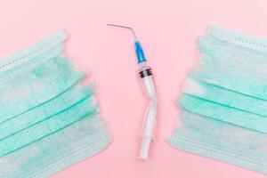 Anti Vaccine Movement and Anti Mask Concept - Broken Medical Syringe and Green Torn Medical Face Mask on the Pink Background. Pandemic and Lockdown End - Top View, Flat Lay photo