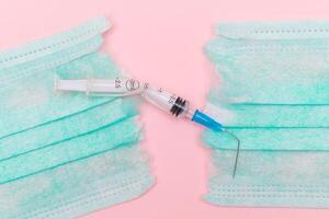 Anti Vaccine Movement and Anti Mask Concept - Broken Medical Syringe and Green Torn Medical Face Mask on the Pink Background. Pandemic and Lockdown End - Top View, Flat Lay photo