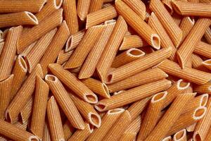 Uncooked Whole Grain Penne Rigate Pasta. A Culinary Canvas of Whole Wheat Macaroni, Creating a Lively and Textured Background for Gourmet Cooking. Whole Grain Dry Pasta. Whole Wheat Raw Macaroni photo