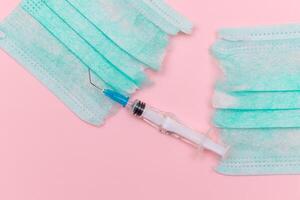 Anti Vaccine Movement and Anti Mask Concept - Broken Medical Syringe and Green Torn Medical Face Mask on the Pink Background. Pandemic and Lockdown End - Top View, Flat Lay photo