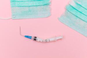 Anti Vaccine Movement and Anti Mask Concept - Broken Medical Syringe and Green Torn Medical Face Mask on the Pink Background. Pandemic and Lockdown End - Top View, Flat Lay photo