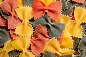 Uncooked Vibrant Colored Farfalle Pasta. A Culinary Canvas of Multicolored Bow-Tie Macaroni, Creating a Lively and Textured Background for Gourmet Cooking Enthusiasts. Colored Dry Pasta. Raw Macaroni photo