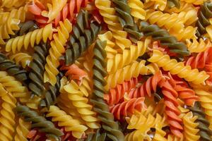 Uncooked Vibrant Colored Fusilli Pasta. A Mesmerizing Culinary Canvas of Multicolored Spirals, Creating a Lively and Textured Background for Gourmet Cooking. Colored Dry Pasta. Raw Macaroni photo