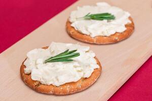 Crispy Cracker Sandwich with Cream Cheese and Rosemary on Wooden Cooking Board on Magenta Background photo