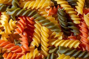 Uncooked Vibrant Colored Fusilli Pasta. A Mesmerizing Culinary Canvas of Multicolored Spirals, Creating a Lively and Textured Background for Gourmet Cooking. Colored Dry Pasta. Raw Macaroni photo