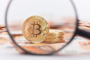 A Stack of Bitcoin Coins Visible Through a Magnifying Glass on the 50-Euro Banknotes. Euro Currency and Crypto Currency. Orange Paper Money. A Lot of Fifty-Euro Bills. Anonymous Payments Concept photo