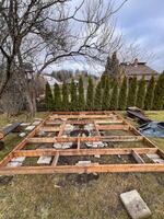 Framework of a wooden deck under construction in a backyard with trees and greenery in the background. photo