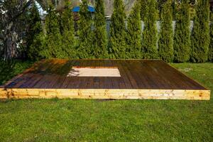 Freshly stained wooden deck with a central sandpit in a backyard surrounded by trees and bushes photo