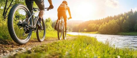 Two cyclists riding on scenic trail beside river during sunset, enjoying nature photo