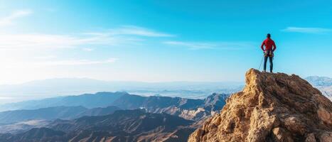 climber stands triumphantly on rocky peak, overlooking vast mountain ranges and clear blue sky. scene captures thrill of adventure and beauty of nature photo