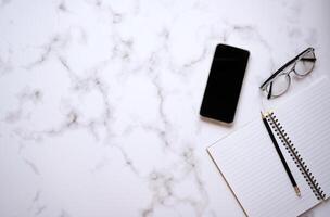 Flat lay top view notebook and pencil with mobile phone and glasses on white color office desk photo