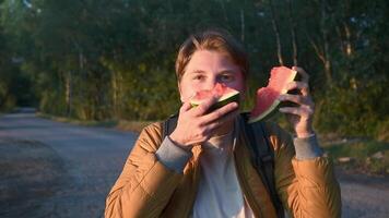 blonde girl with short hair like a boy appetizingly bites two pieces of watermelon at once and laughs, portrait in the sunny golden hour at sunset in the forest,full connection with nature, video