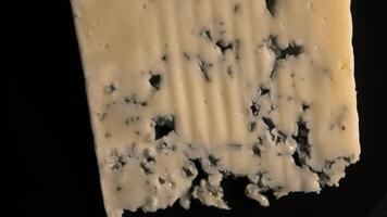Blue cheese rotating on black background, top view video