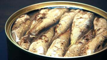 Fish in a can of oil rotates on a black background, close-up. Sprats. Seafood video