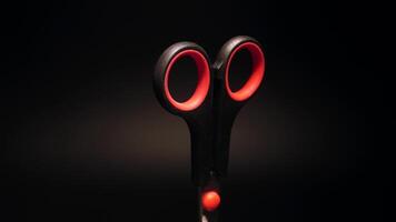Scissors with red handles rotate on a black background video