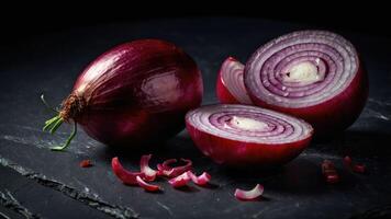 A red onion, whole and sliced, displayed on a dark surface for culinary purposes. photo