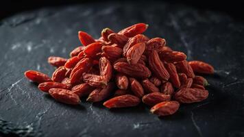 A pile of dried goji berries on a dark stone surface, showcasing their texture and color. photo