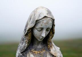 Weathered stone statue of a cloaked figure with a serene expression photo