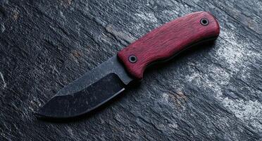 Closeup of a sharp folding knife with a red wooden handle on a dark slate background photo