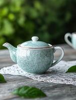 Vintage ceramic teapot on lace doily with green leaves photo