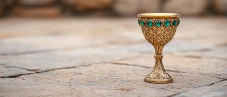 Ornate golden chalice with emerald gems on a wooden surface photo
