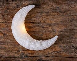 Crescent moon made of ice on wooden background photo