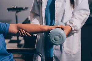 Old woman training with physiotherapist using dumbbells at home. Therapist assisting senior woman with exercises in nursing home. Elderly patient using dumbbells with outstretched arms. photo