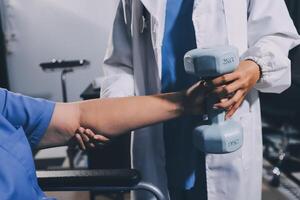 Old woman training with physiotherapist using dumbbells at home. Therapist assisting senior woman with exercises in nursing home. Elderly patient using dumbbells with outstretched arms. photo