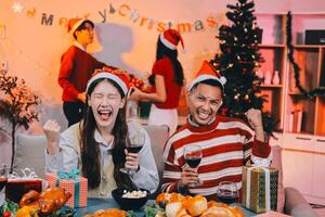 Group of happy Asian friends celebrating Christmas and decorate the Christmas tree indoors. Beauty woman with Christmas Gifts. New Year party. Woman hands decorate Christmas tree red ball, bauble. photo