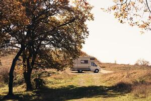A serene camping spot with a camper van under autumn trees in the countryside during daylight hours photo