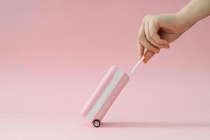 Creative trendy layout made with pink suitcase and woman's hand on pastel pink background. Minimal travel concept. Fancy vacation idea. photo
