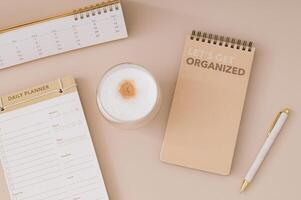 Trendy layout with daily planner, calendar, coffee and pen on beige background. Planner for organization and goal priorities. Writing down tasks and schedule reminders on office desk. Minimal concept. photo