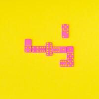 Pink dominoes on yellow background. Minimal board game concept. Trendy tile based game idea backdrop. Colorful domino flat lay. photo