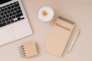 Trendy layout with planner, computer, coffee and pen on beige background. Planner for organization and goal priorities. Writing down tasks and schedule reminders on office desk. Minimal concept. photo