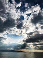 Dramatic cloudy sky over calm ocean with sunlight peeking through photo