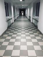 Long empty corridor with checkerboard tiled flooring and windows photo