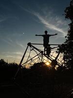Silhouette of a child playing on a climbing frame at sunset photo
