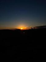 Silhouette of two people enjoying a sunset on a hill photo