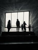 Family silhouette standing by large window in dark hallway photo